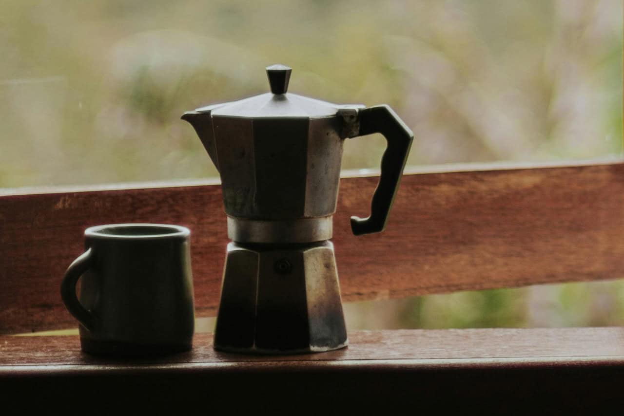 eine Kaffeetasse steht an einem Fenster, draußen ist viel Grün zu sehen